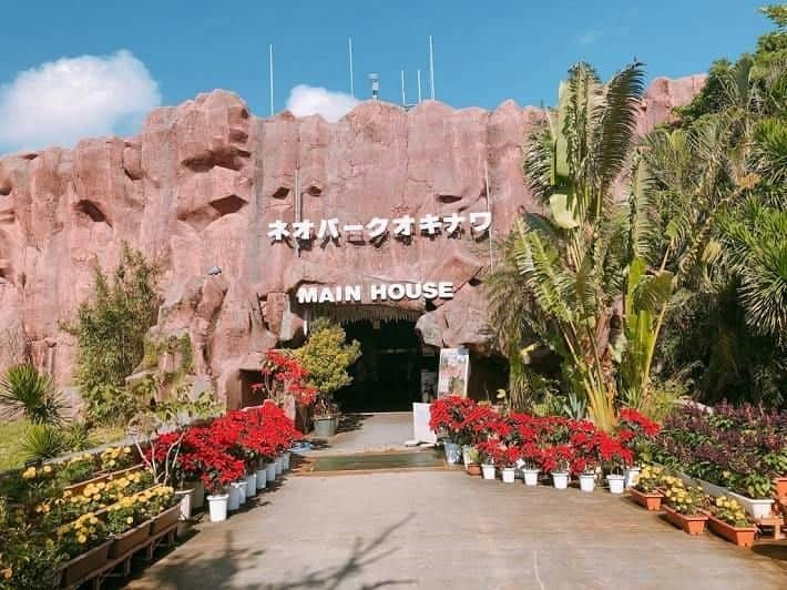 A rocky building facade with the text 'Main House' above the entrance, surrounded by vibrant plants and flowers.