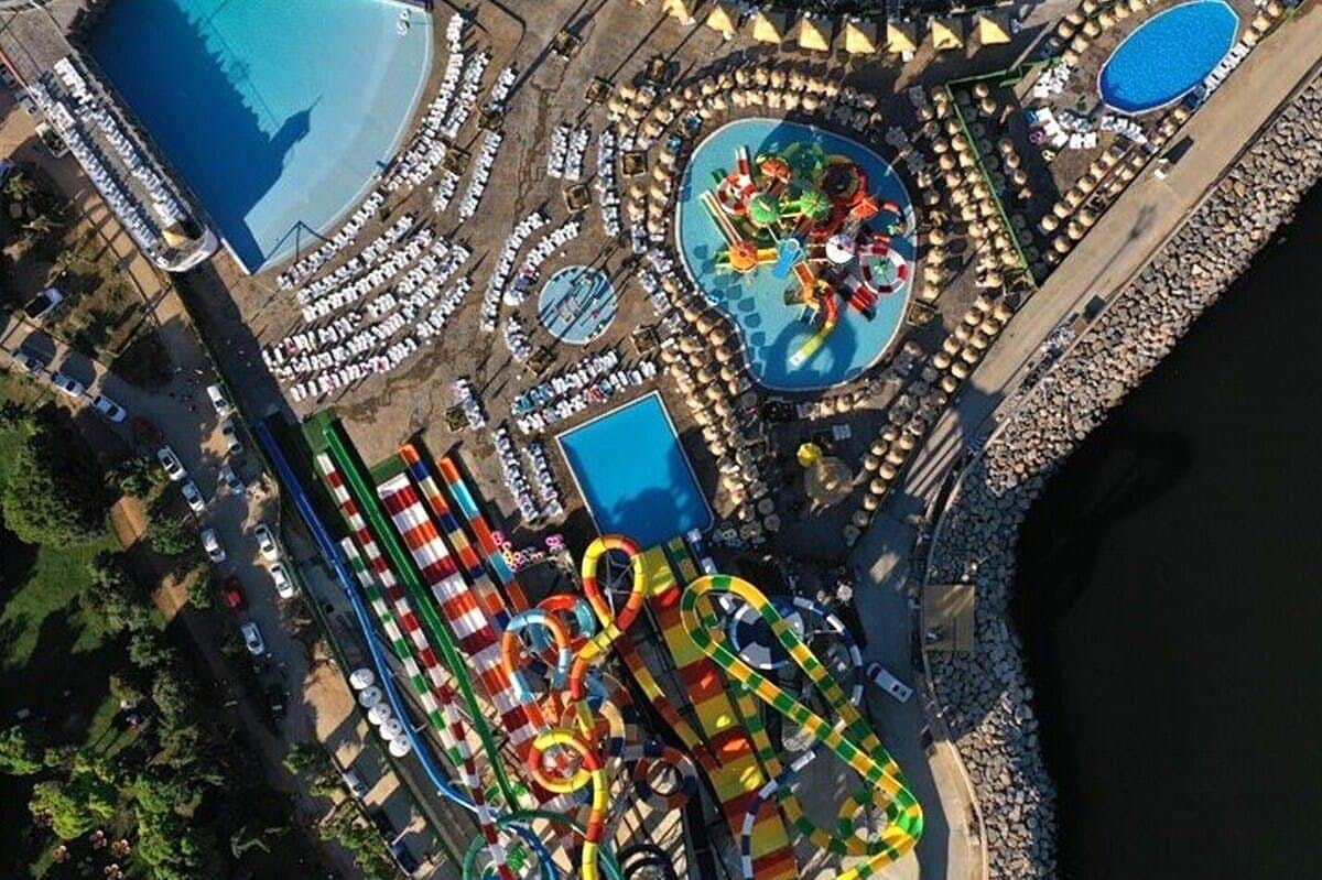 Viaport Marina Aquapark: Entry Ticket + Optional Hotel Transfer Aerial view of a waterpark with colorful slides, pools, sunshades, and lounge chairs arranged around the area.