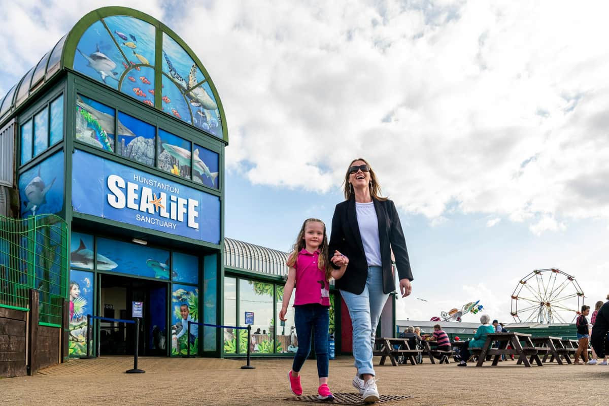SEA LIFE Hunstanton: Entry Ticket A woman and a child walk hand in hand outside the Hunstanton SEA LIFE Sanctuary. Other visitors and a Ferris wheel are visible.
