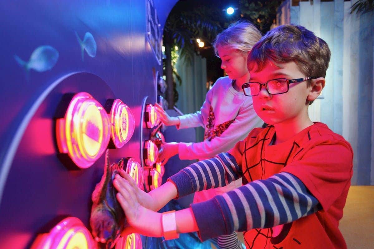 SEA LIFE Scarborough: Entry Ticket Two children, one in a striped shirt and the other in a pink shirt, interact with a wall of colorful, illuminated buttons.