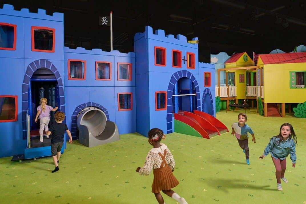 SEA LIFE Michigan & Peppa Pig World of Play: Entry Ticket Children playing in an indoor play area featuring colorful castle and house structures with slides and green flooring.