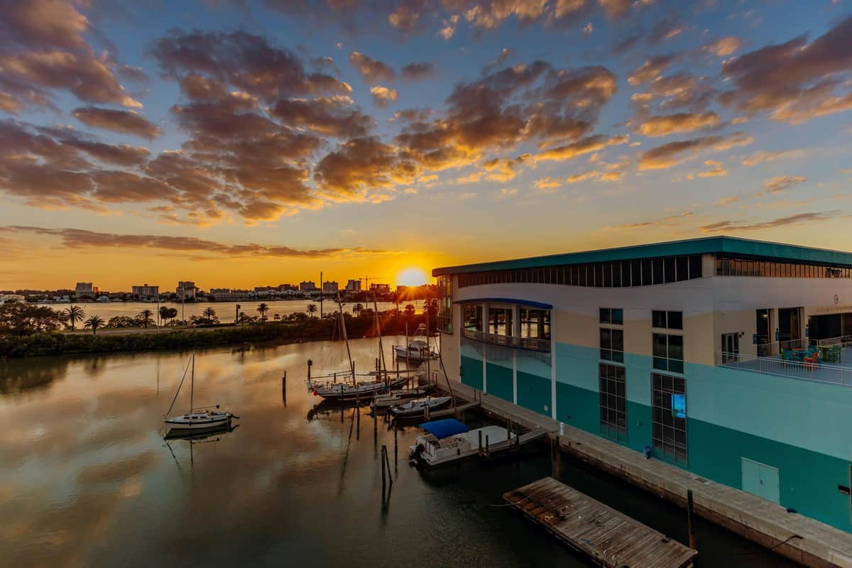 Clearwater Marine Aquarium: Entry Ticket Sunset over a marina with sailboats docked by a modern building, calm waters, and scattered clouds in the sky.