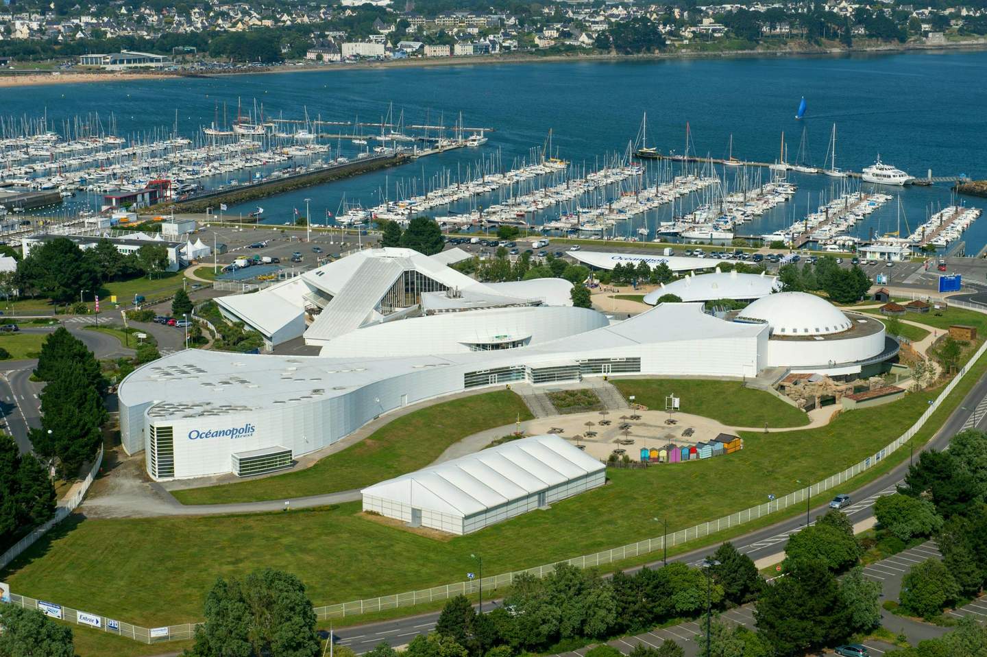 Océanopolis Aerial view of Océanopolis, a coastal complex with white buildings and a marina filled with boats, set by the water.