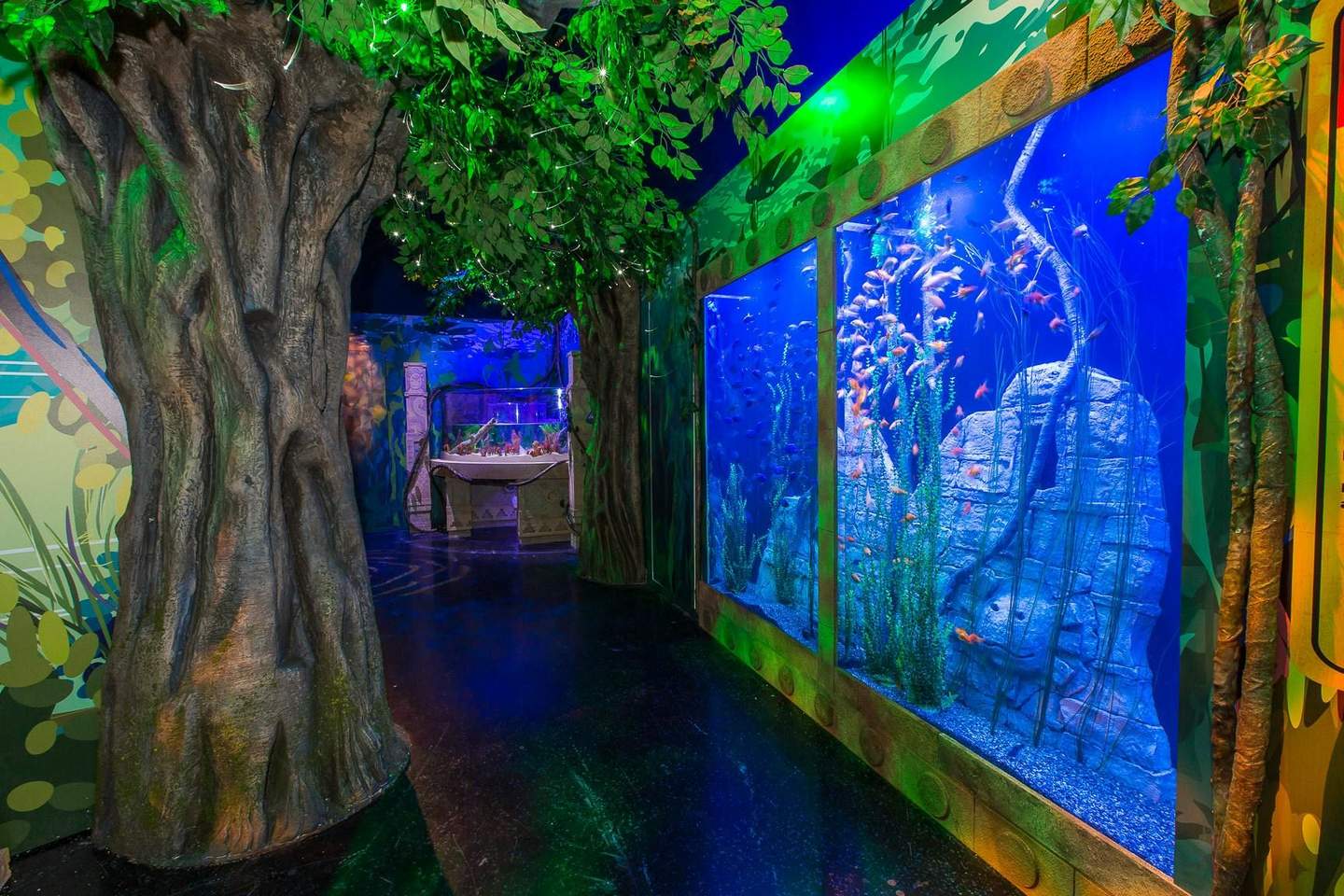 SEA LIFE Orlando An indoor aquarium with large fish tanks, tree-like structures, lush green foliage, and vibrant lighting in a jungle-themed setting.